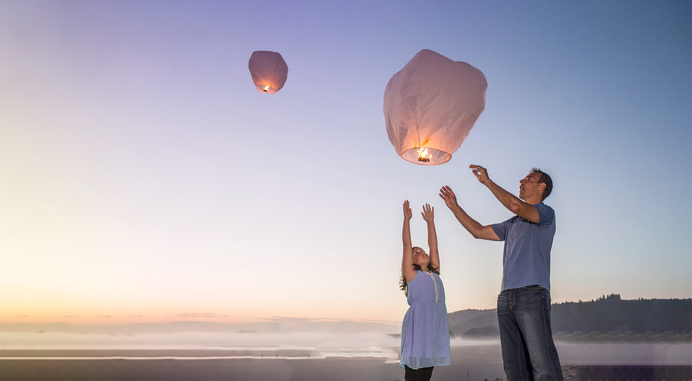 Tată și fiică care lansează lampioane pe plajă la apus