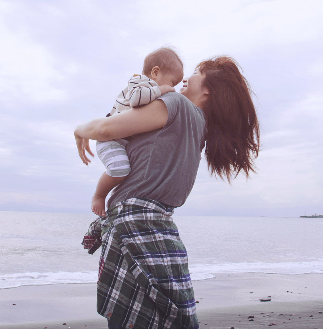 Mamă ținându-și copilul în brațe pe malul mării